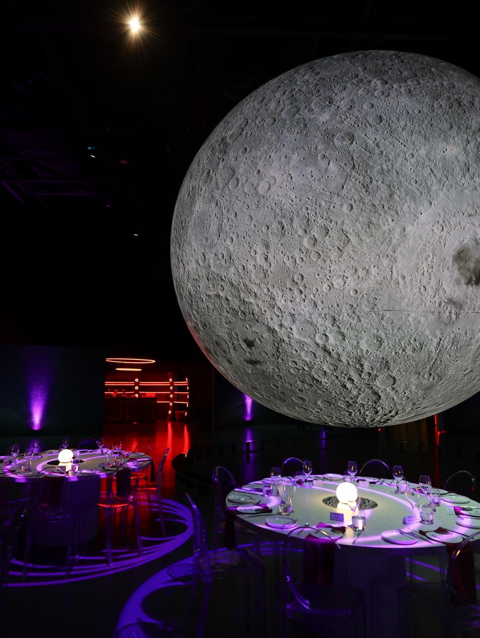 Glowing large Moon setup above four round dinning tables