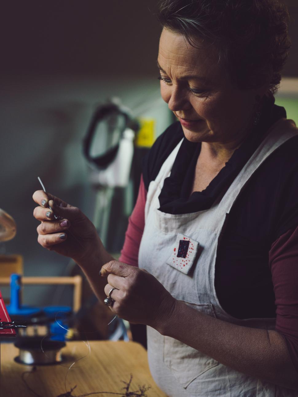 An adult in a workshop holds an art tool with wire attached to it. They are concentrating on what they are doing.