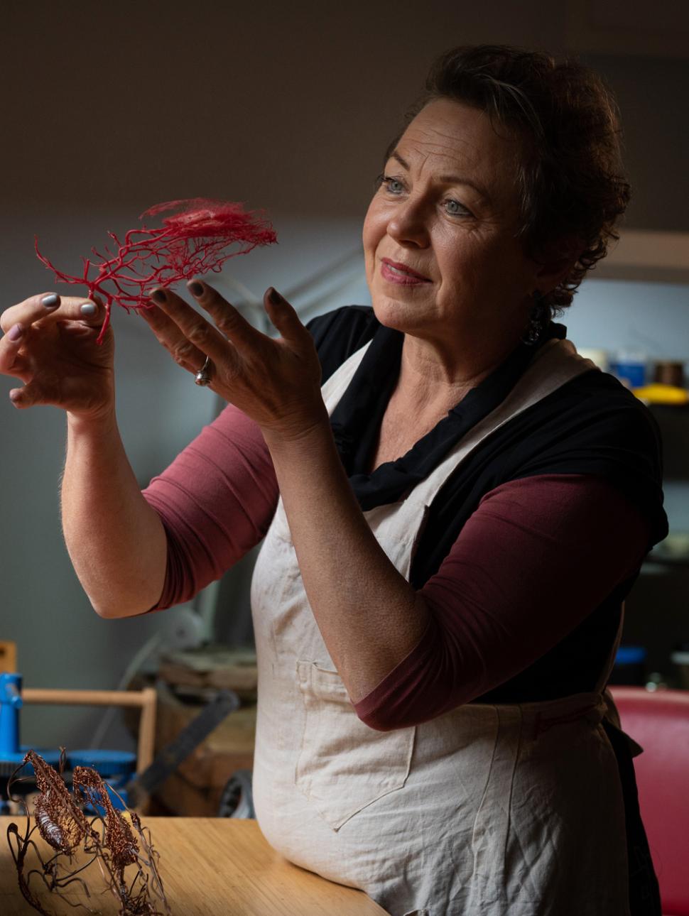 An adult in an artist workshop holds up a delicate piece of artwork to the light and is looking at it intently