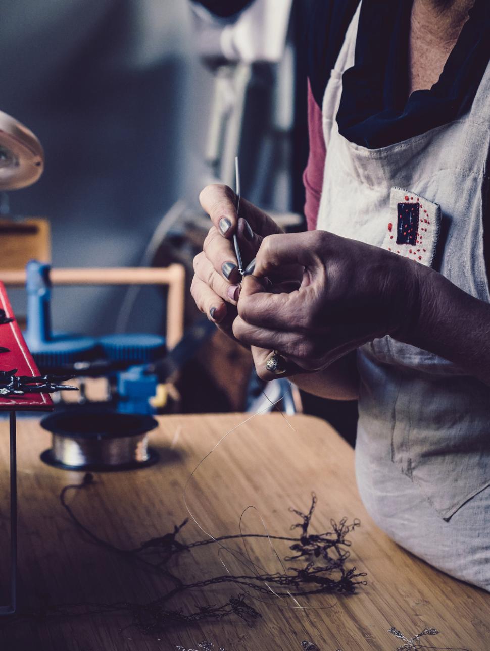 a close up of hands delicately creating an artwork with jewellery in a workshop