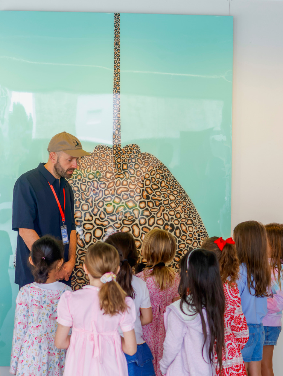 Artist Ian Daniell stands in front of a colourful artwork with a group of children