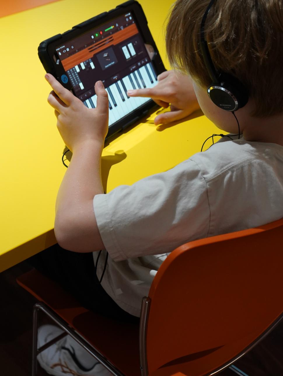 Image is looking over a boys shoulder while he is using an iPad with the GarageBand program to create music.