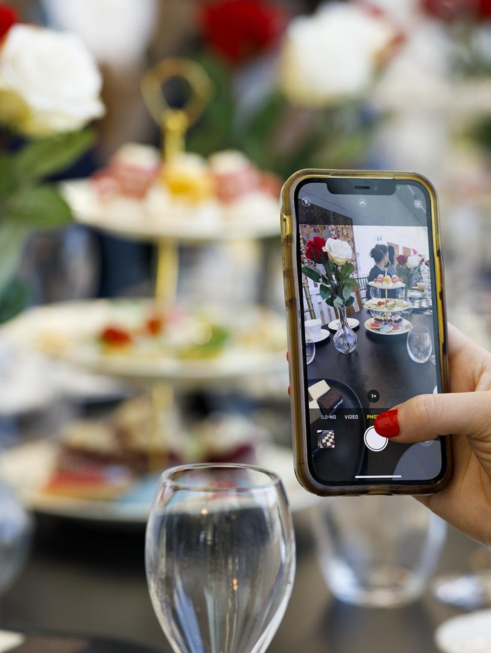 a high tea setup with someone using a phone camera and taking a picture 