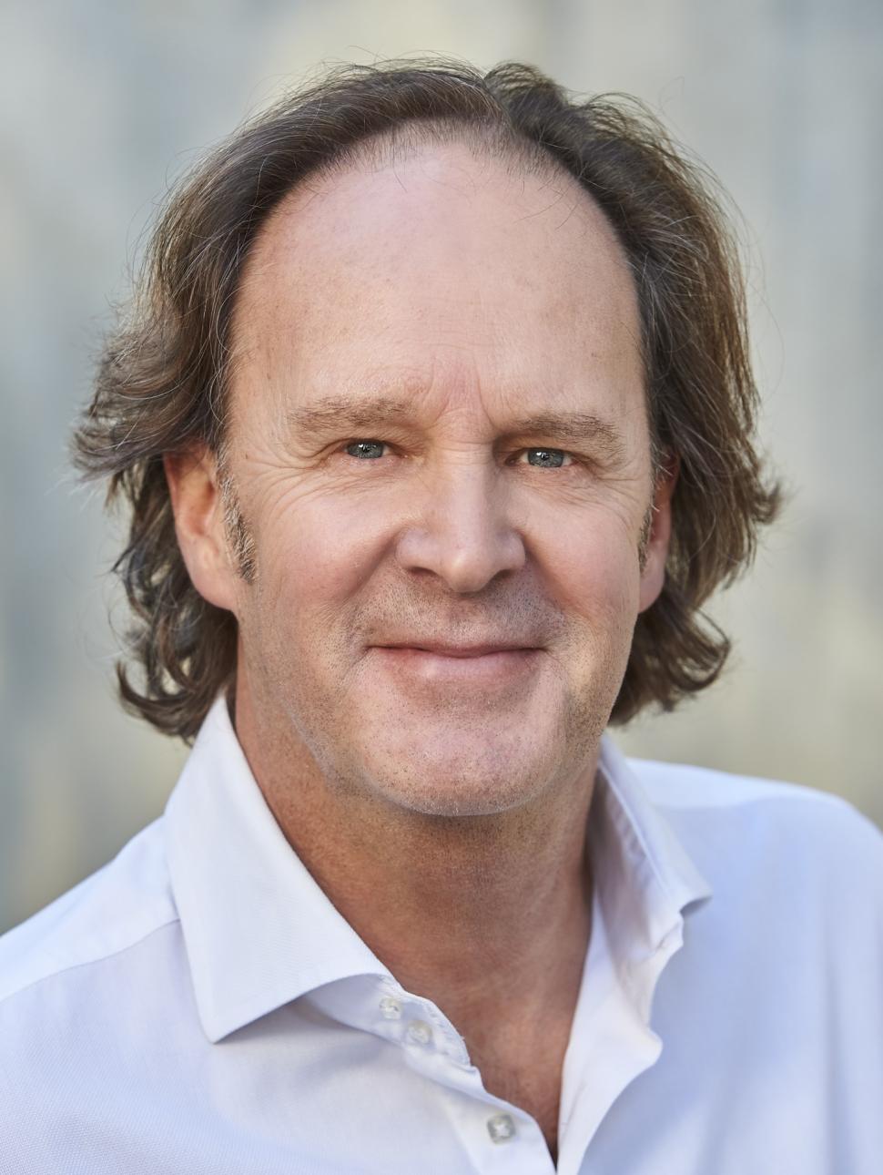 a middle aged white man with brown hair wearing a white shirt and looking at the camera