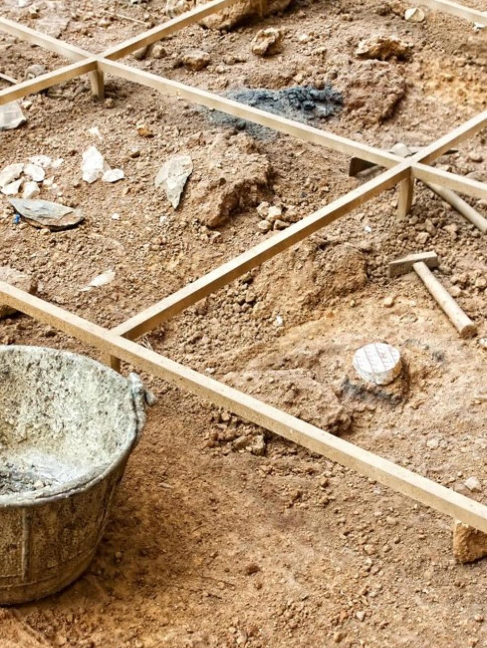 This image shows a close up section of an archaeological dig site. You can see a wooden grid demarcating the area and some tools. 