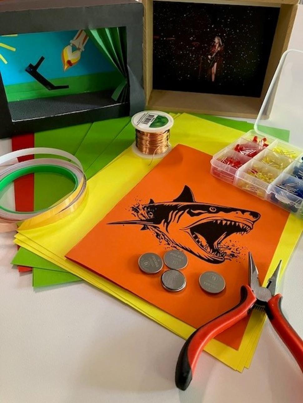 A range of materials are displayed on a table top. There is coloured card, LED lights, coin cell batteries , copper tape and some mini pliers. These will be used to create a small theatre using an electrical circuit to create lighting for the theatre.