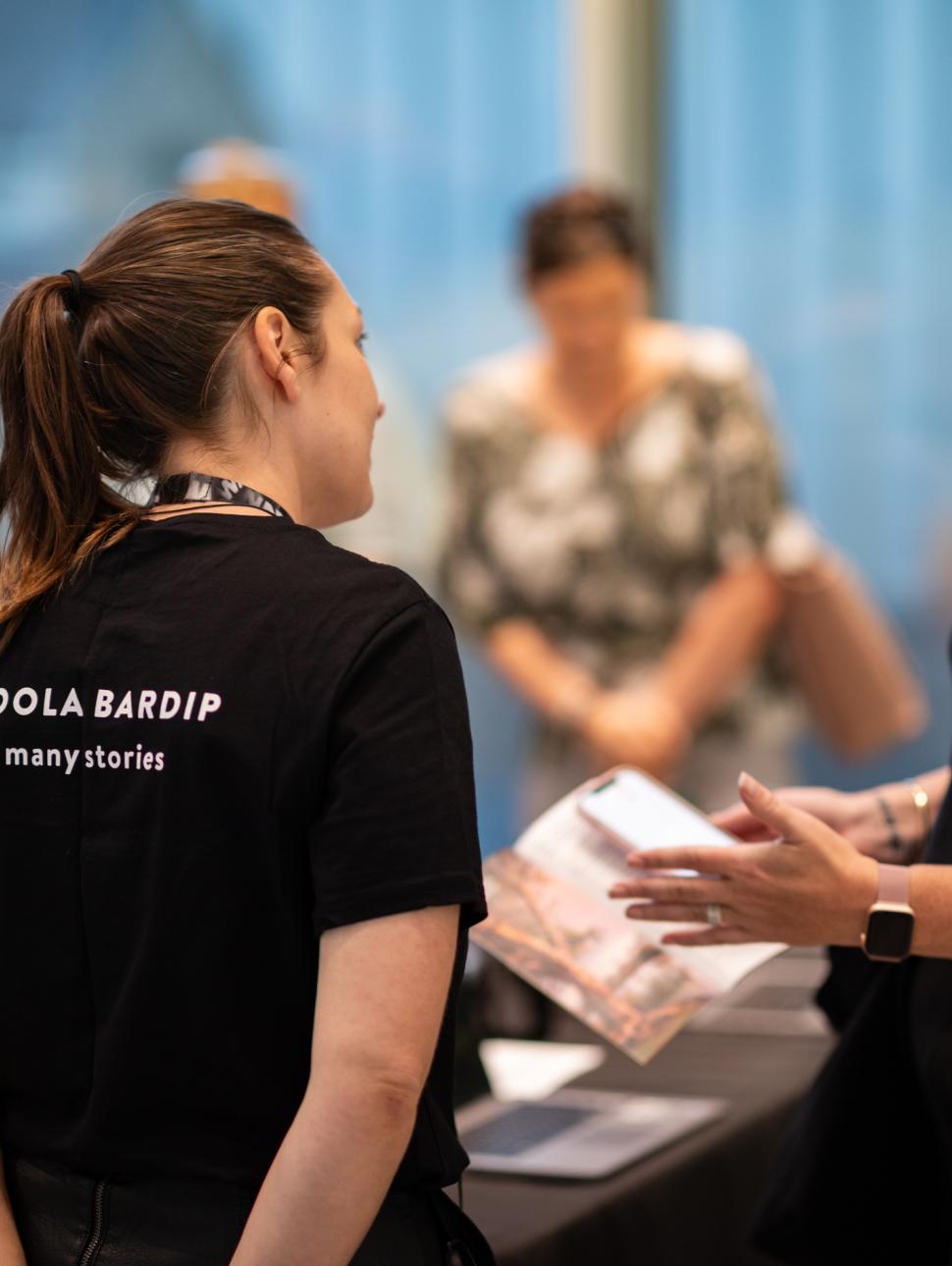 Two women talking, one in Boola Bardip shirt with back to camera