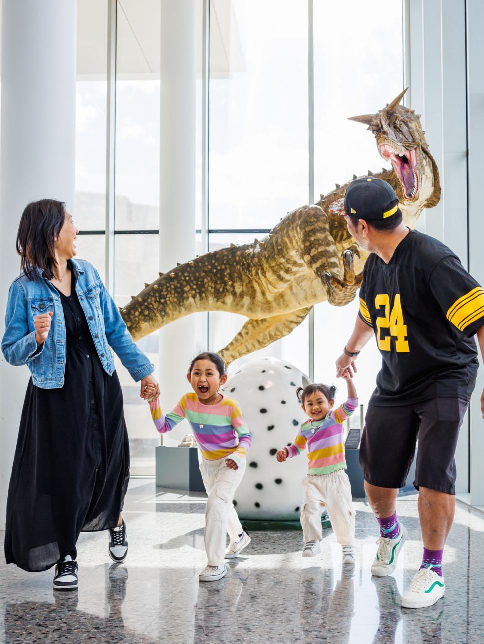 A family of four running away from a dinosaur exhibit in a Museum 