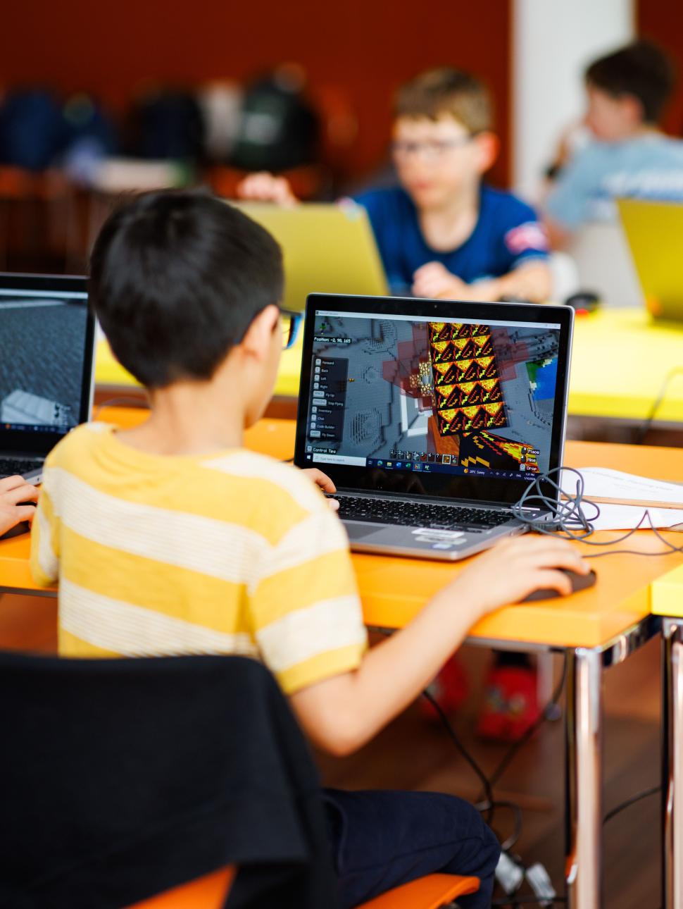 The image is looking over the right hand shoulder of  a young person using a laptop to play Minecraft