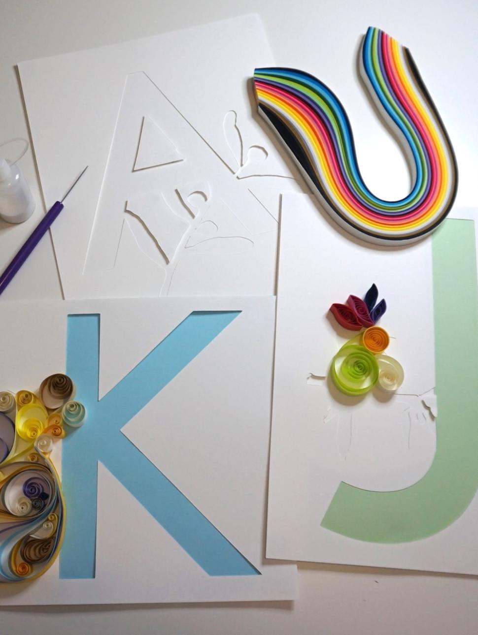 The image shows several items used in the craft of quilling. In particular strips of coloured paper, a quilling tool and the letter K and J letter templatescoloured s