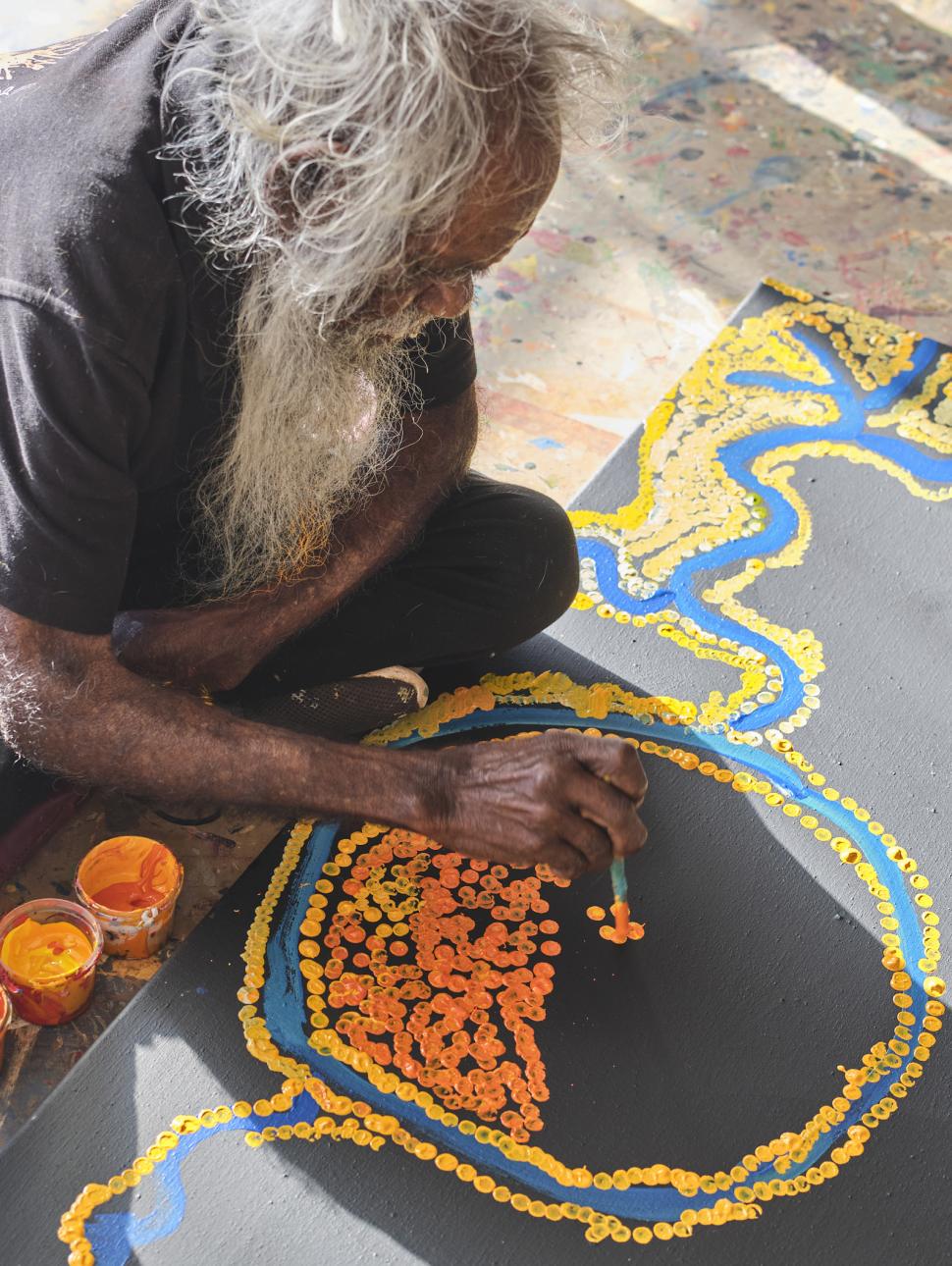 Aboriginal artist painting on the floor with bright colours