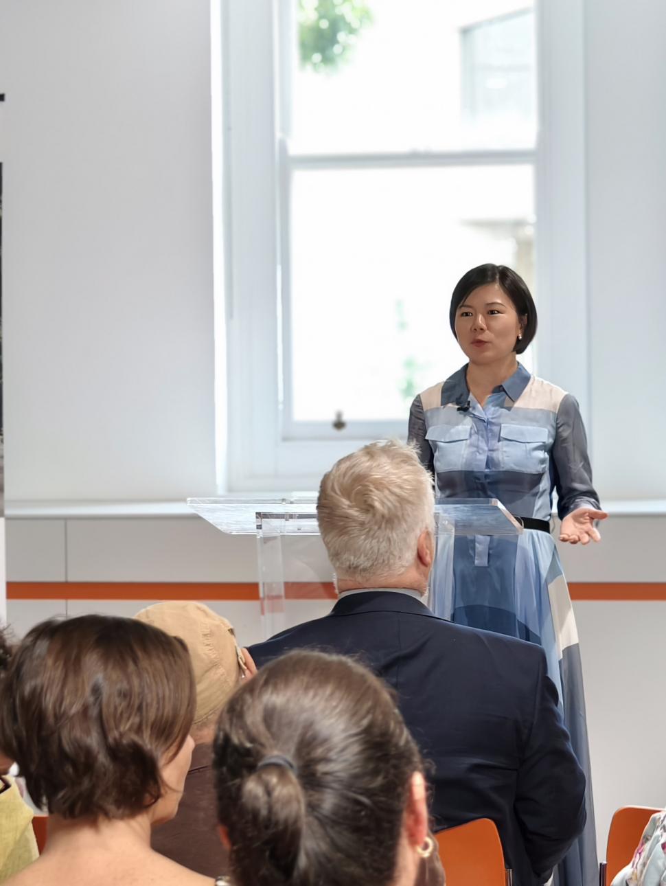 A woman of Asian decent stands at a podium speaking to a crowd