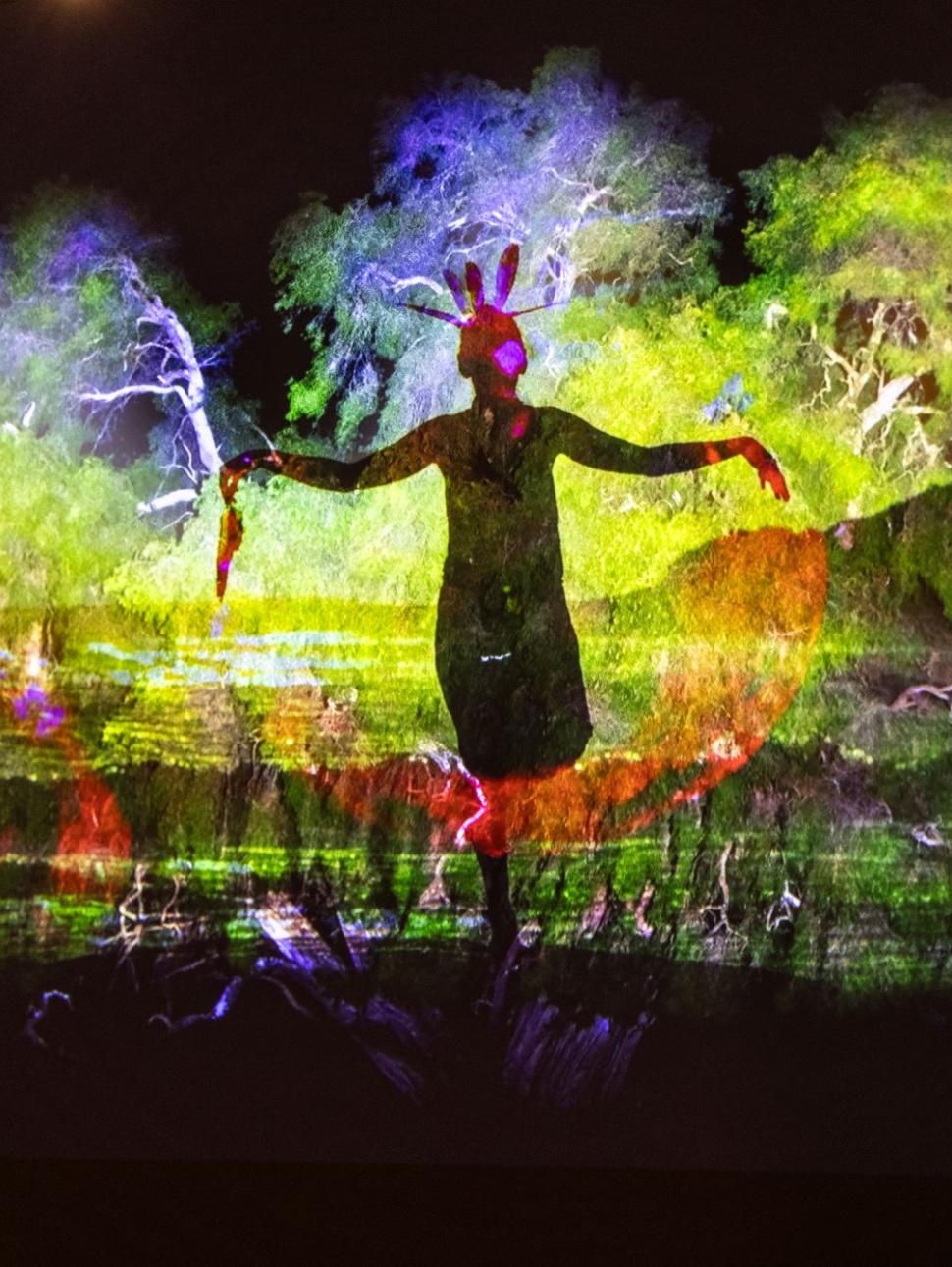 A vibrantly-coloured yellow and green image featuring the silhouette of a person with their arms outstretched and vibrant hazy images of green trees