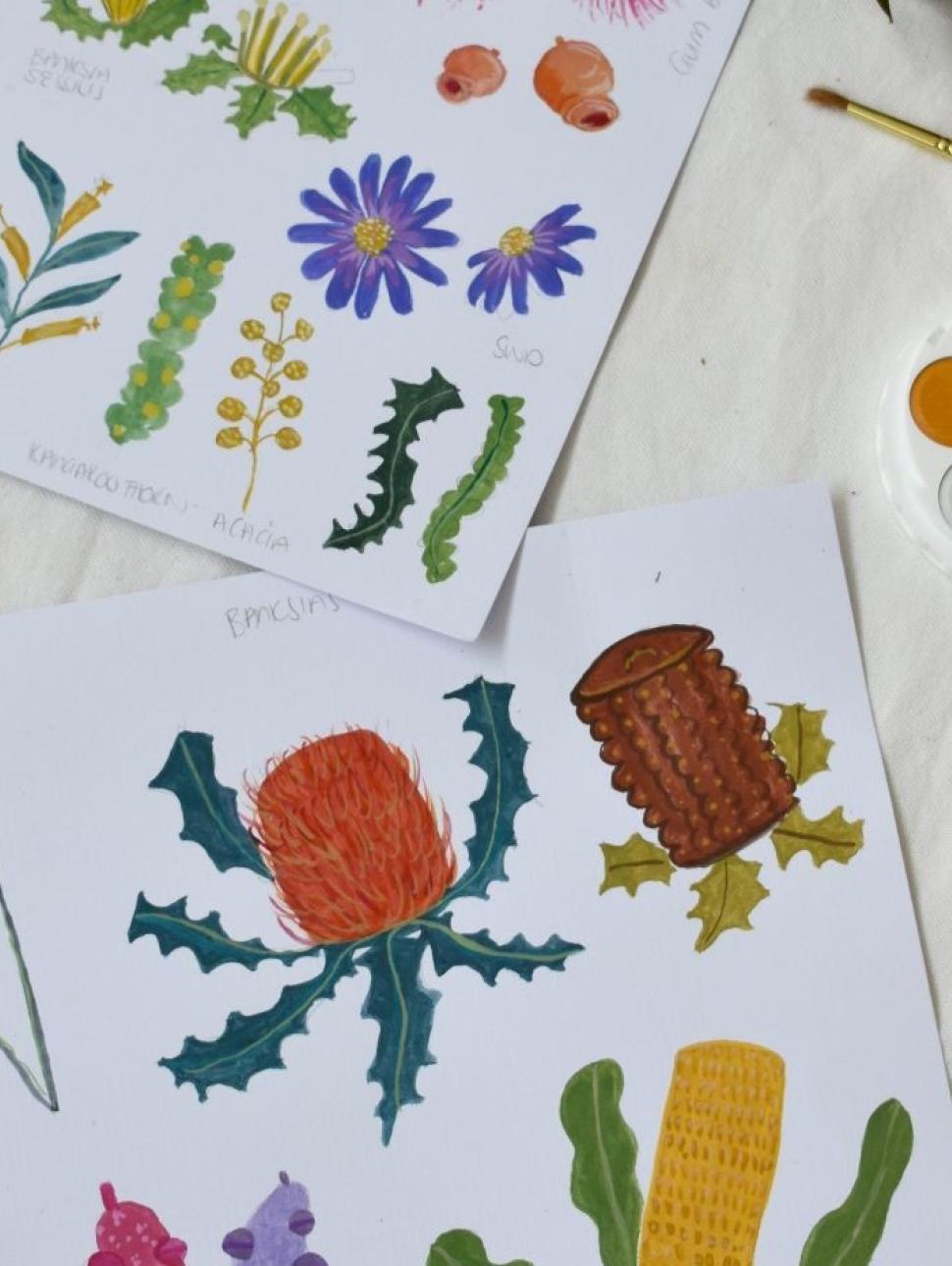 Two pages of watercolour paintings of vibrant Australian botanicals on a white table with a paintbrush and paint palette. 