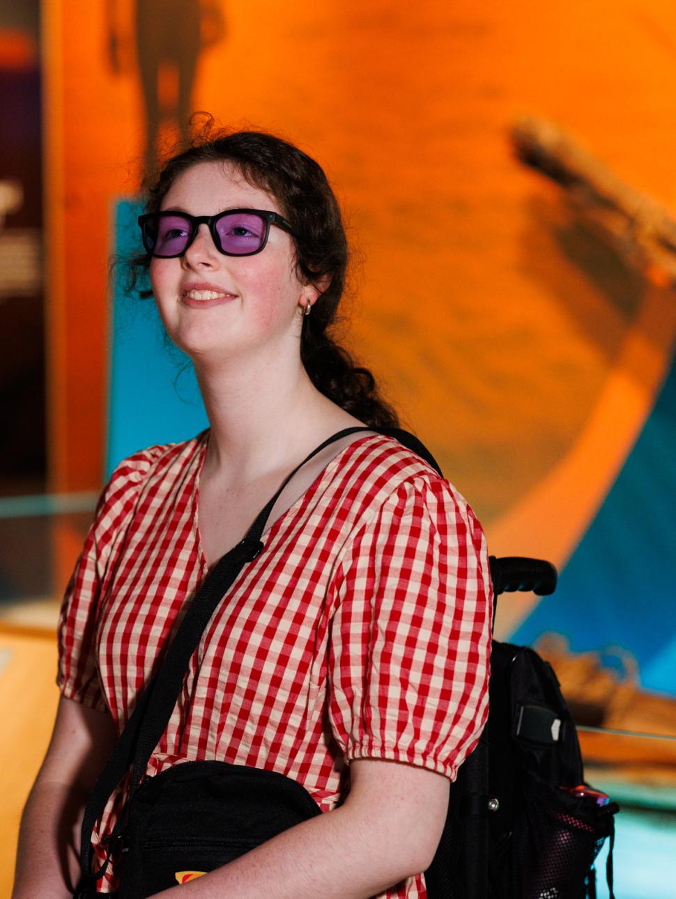 A smiling girl wearing colour blind glasses looking up in awe at a museum exhibit.