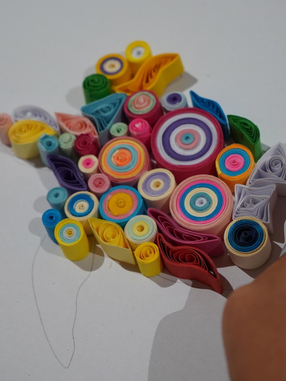 Quilling involves the rolling of strips of paper into shapes and then creating a piece of artwork with them. This images shows a piec eof artwork being created using many different colours and shapes of quills. 