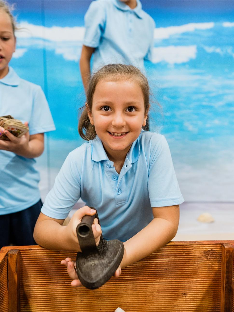 A girl student holds an antique iron during an education program session of Shipwrecked at WA Shipwrecks Museum