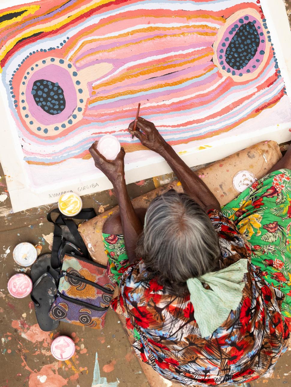 Aboriginal artist painting on the floor with bright colours