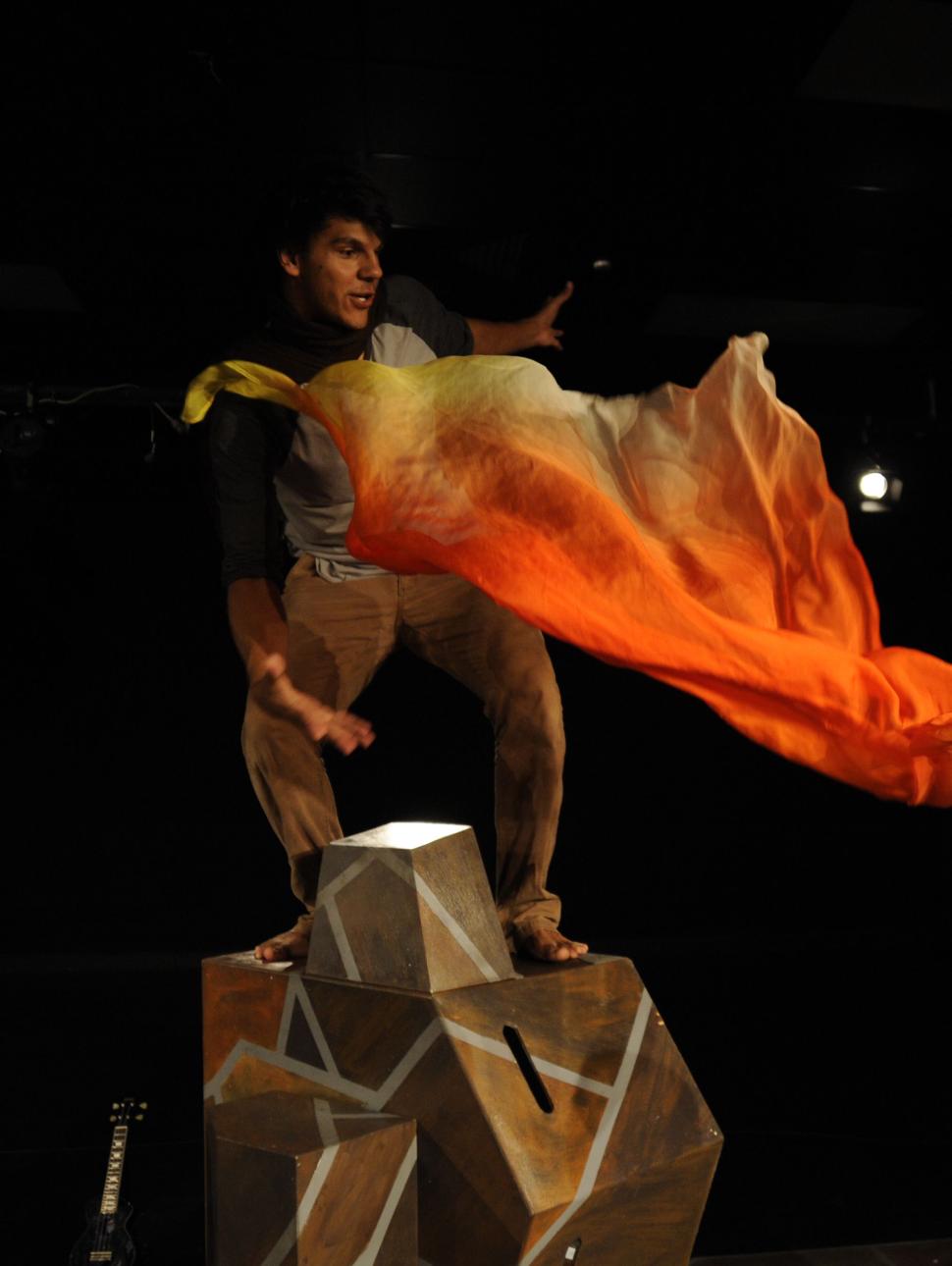 Yirra Yaakin Theatre Company presents Kaarla Kaatijin, a performance for young people about Noongar country and the importance of fire knowledge. This scene features a performer standing high on staging and reacting to a flame-coloured waft of fabric in a dynamic action moment.