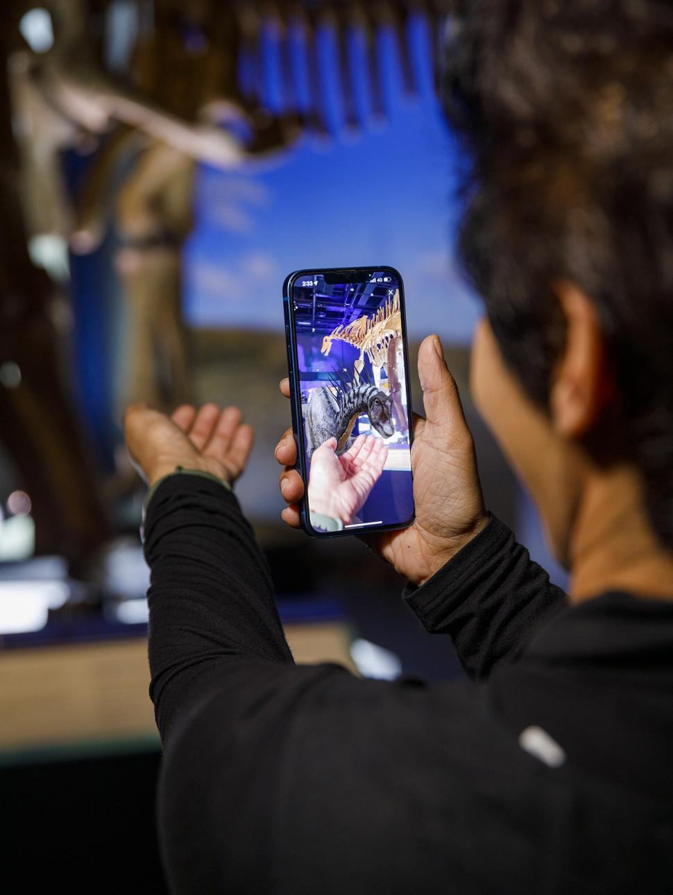 A person holding a phone looking with a 3D dinosaurs featured