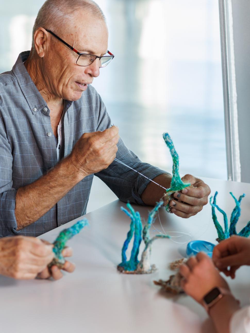 A small group are shown sewing ghost net materials into marine fauna project elements for a Maritime Crafternoon ghost nets art activity workshop.