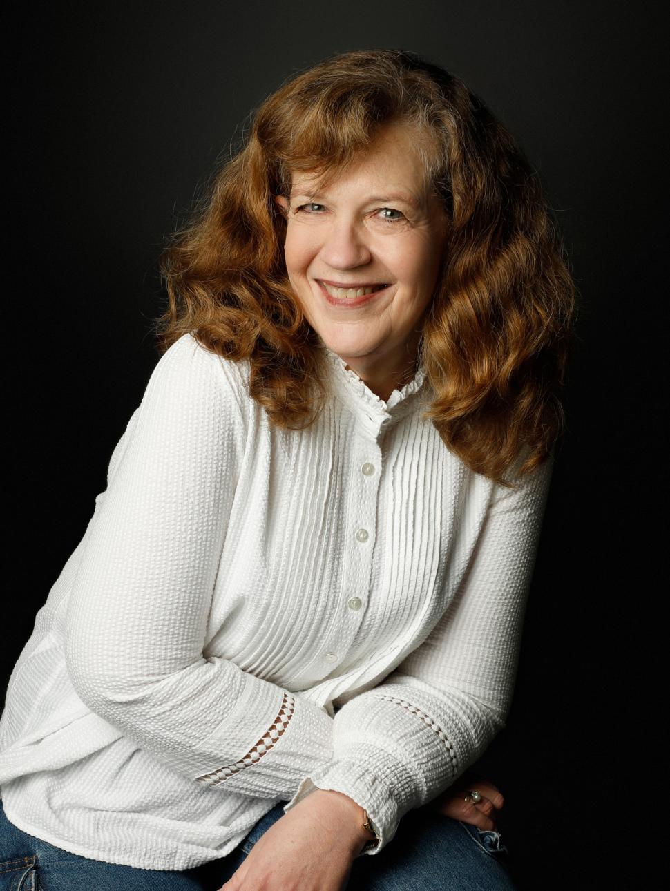 a headshot of a person with a warm smile. They wear a white top and jeans