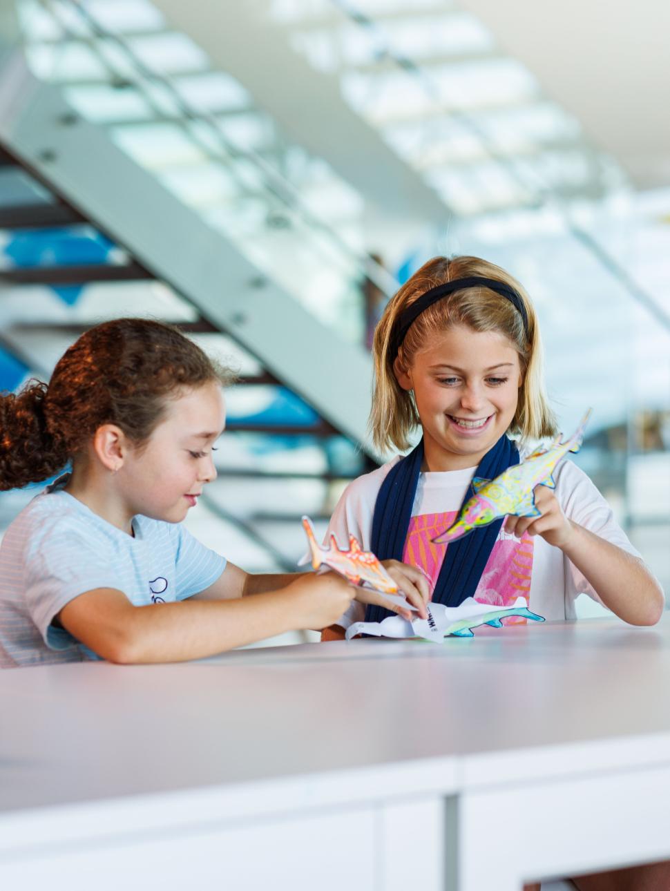 Two girls playing with sawfish finger puppet colouring at the WA Maritime Museum for July 2025 school holidays.