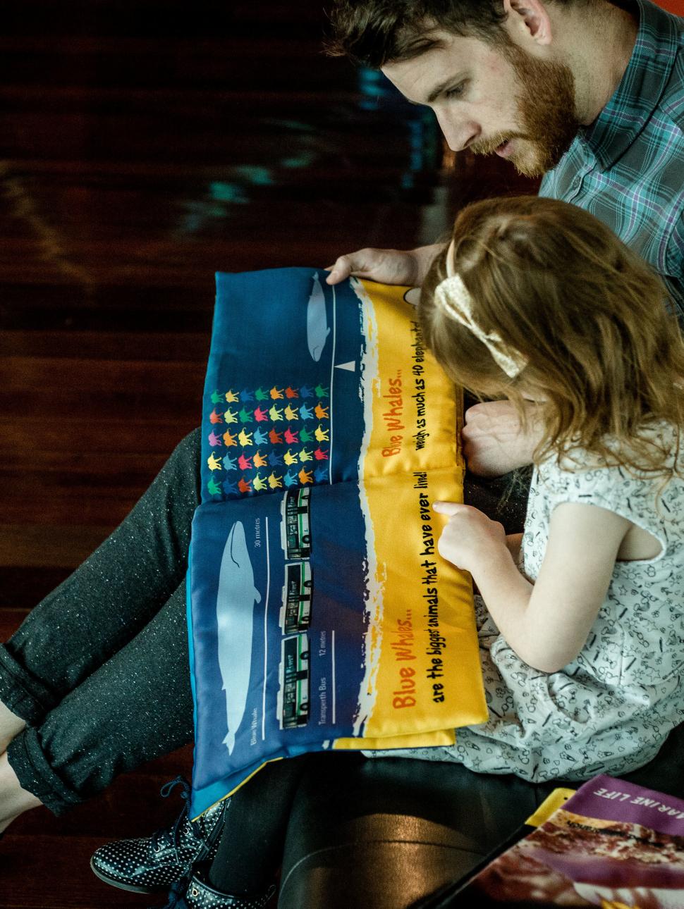 a young child and reads a sea story book with an adult next to them guiding them