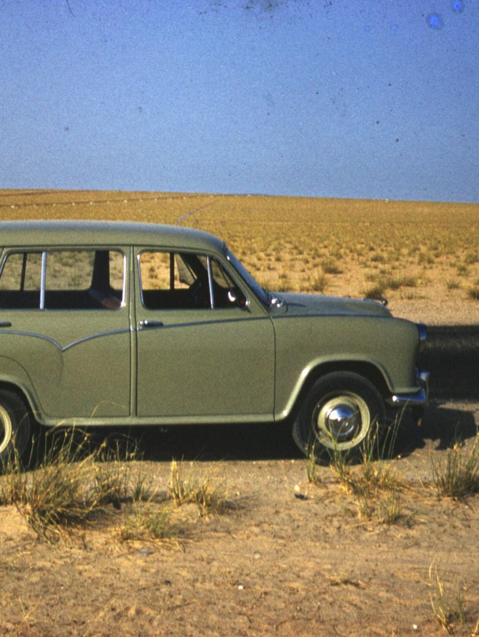 a green car from the 1960s on a dirt road in a nature landscape with only shubs