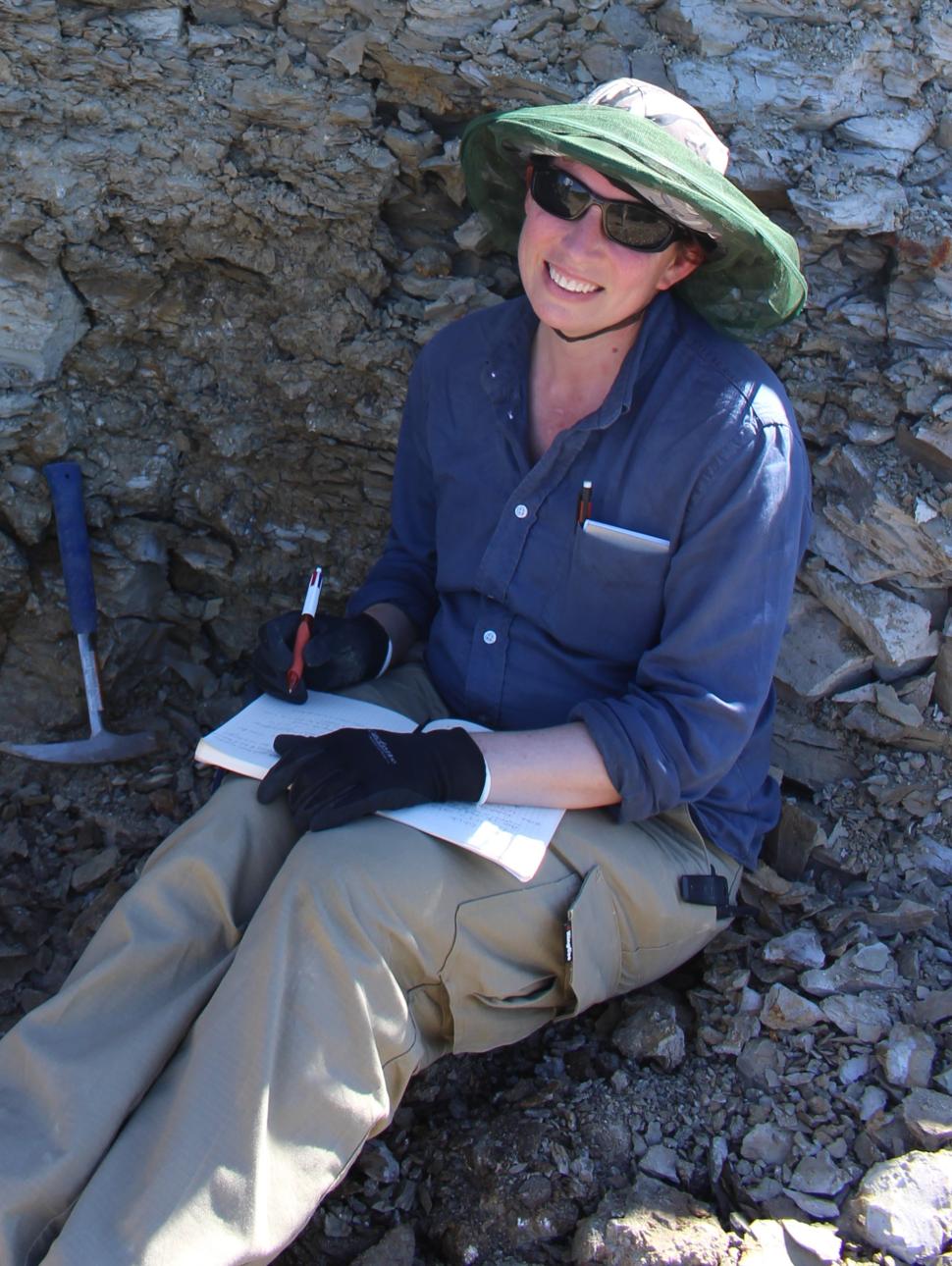 a person sits in a pit of rubble with picks and takes notes on her book.