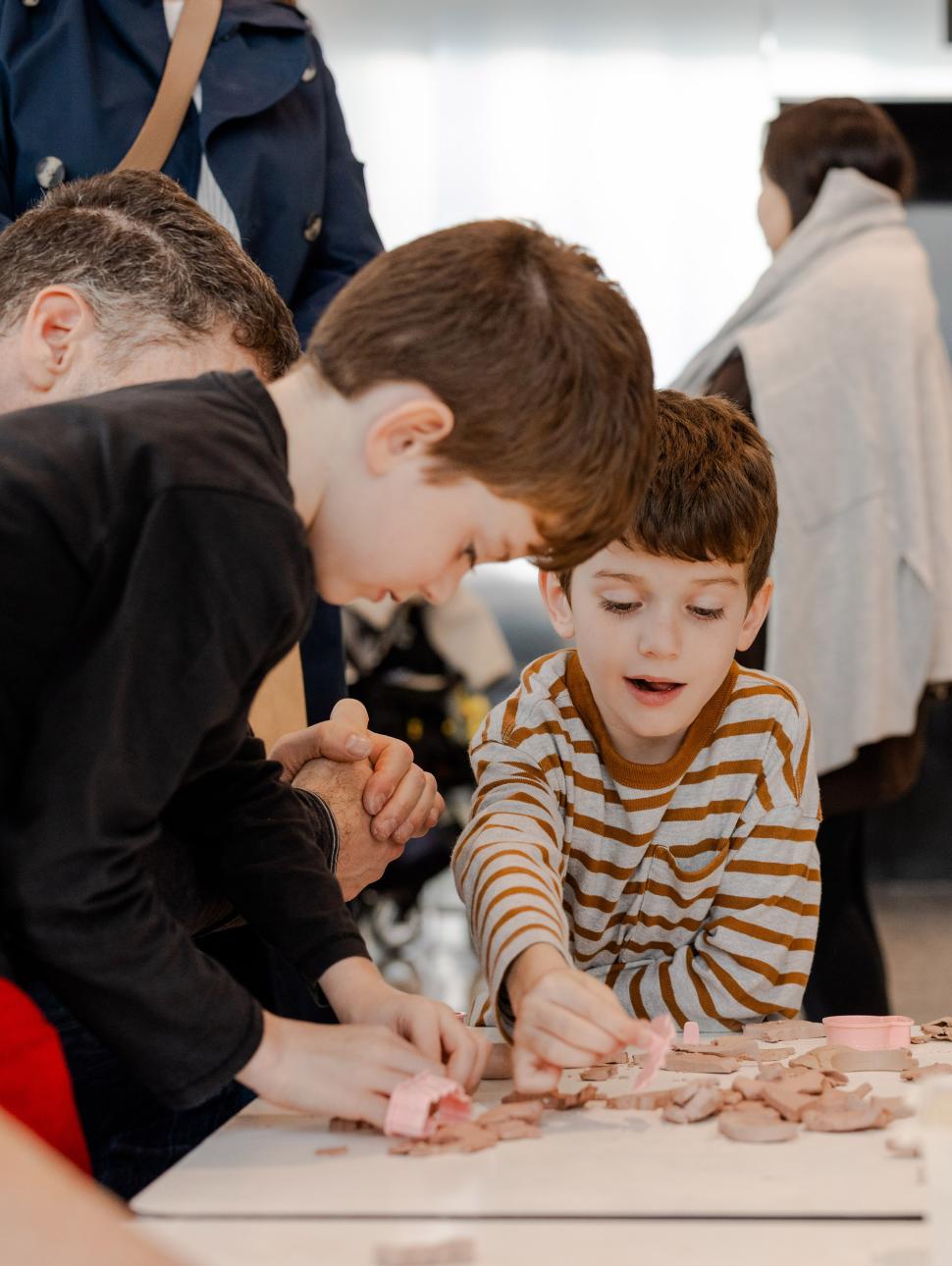 Two young boys gather around a table, happily shaping and playing with clay in a creative activity.