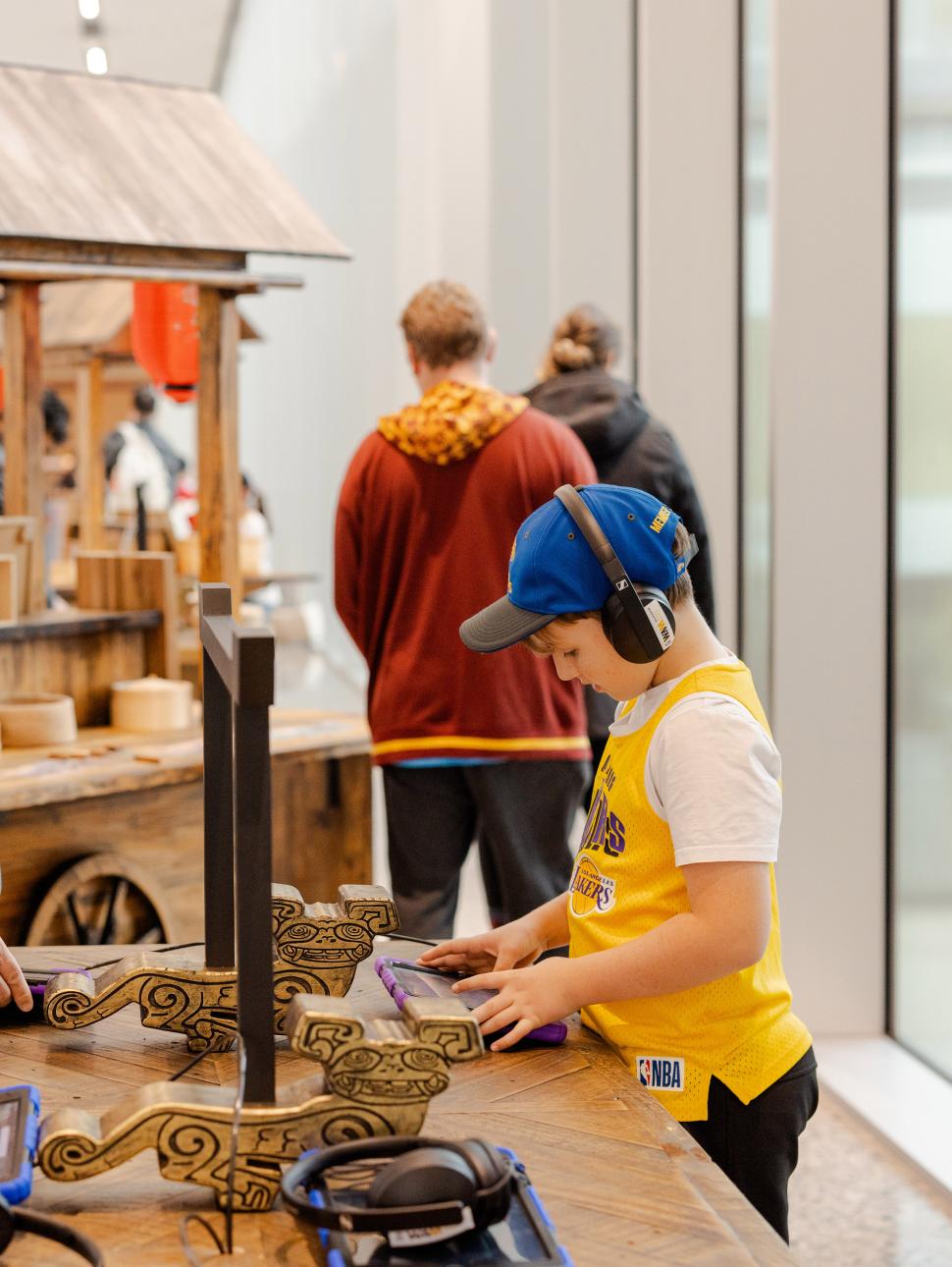 A young boy with headphones on listens to various sounds while playing with GarageBand on an iPad, surrounded by Chinese inspired wooden carts