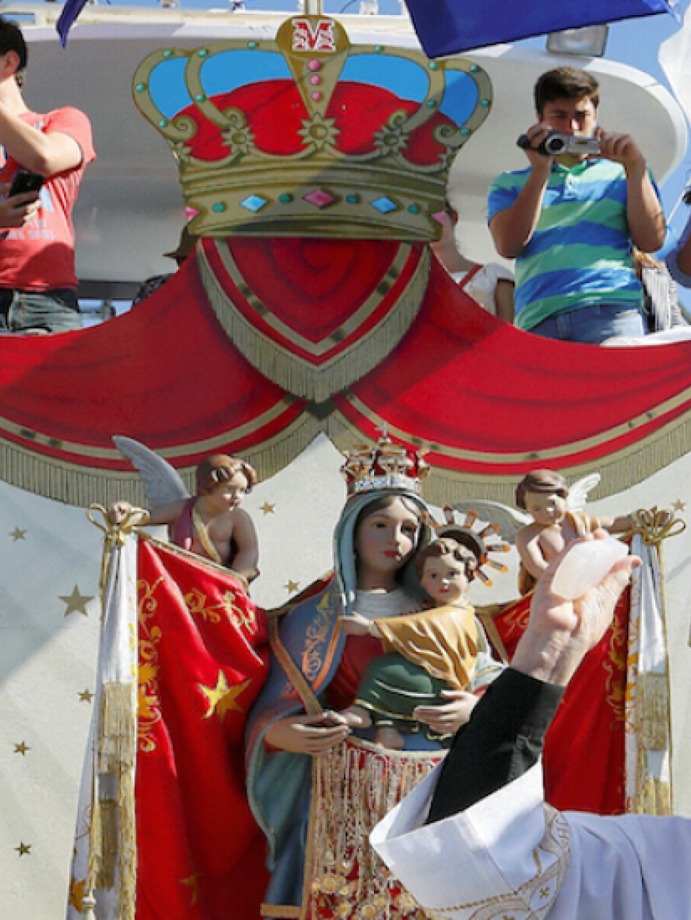 Priest, officials and festival goers on a boat being blessed on a sunny day