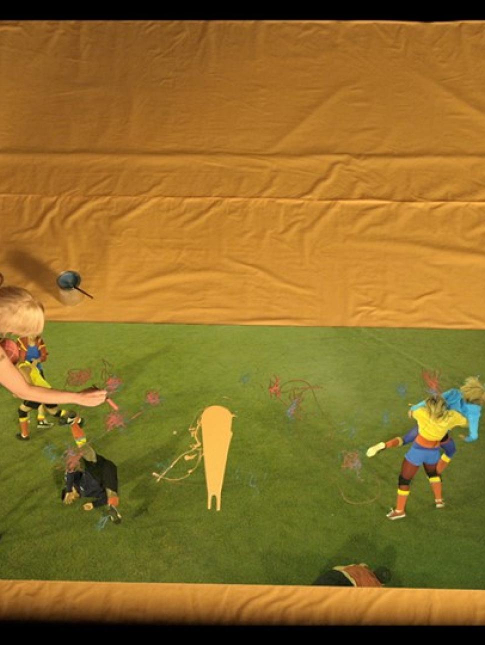 Artist painting on green paper on the floor with a variety of coloured paints and superimposed digital images of young people interacting on a sports field