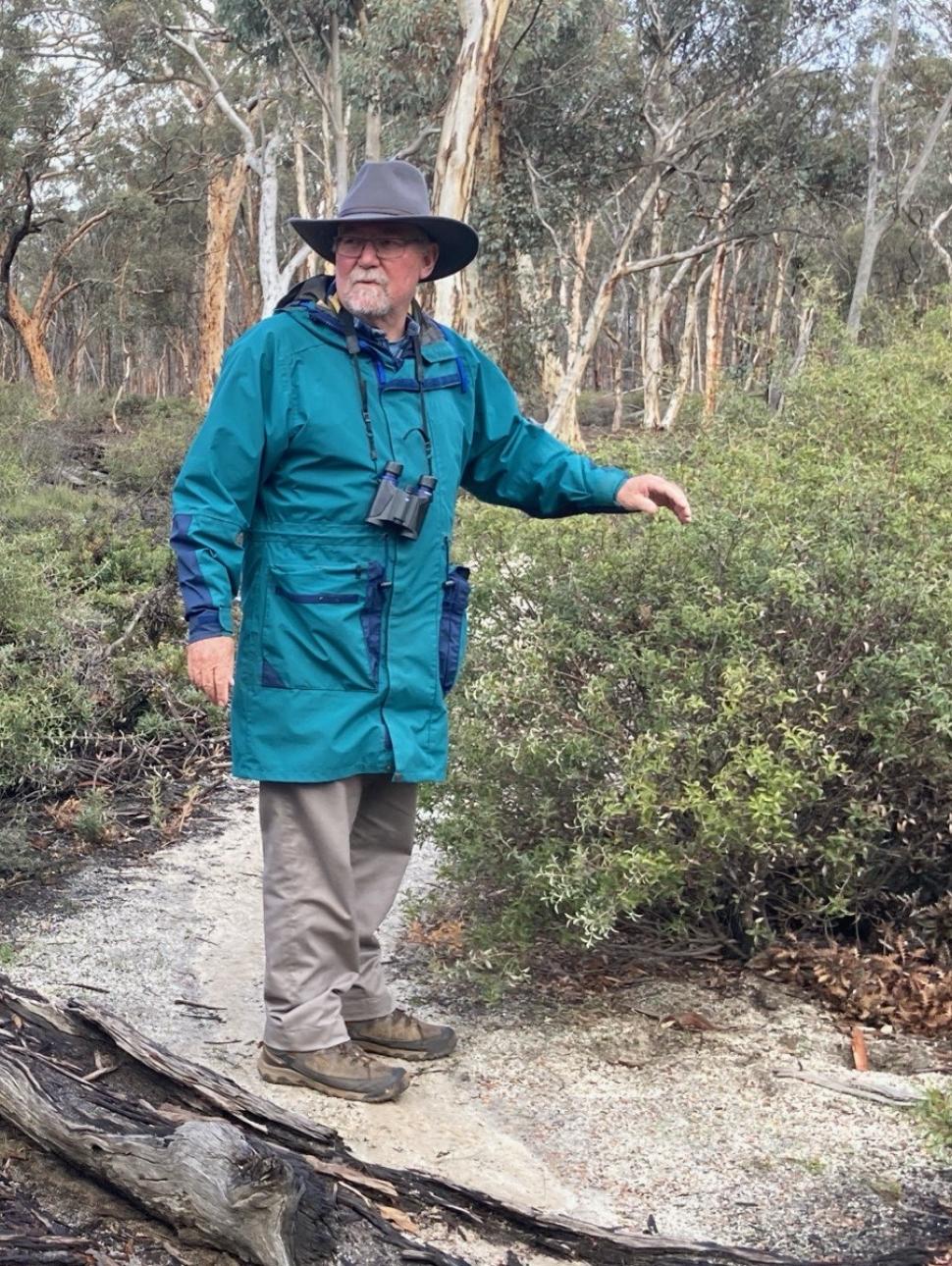 a person is out in the bushland with a hat on and has binoculars around their neck
