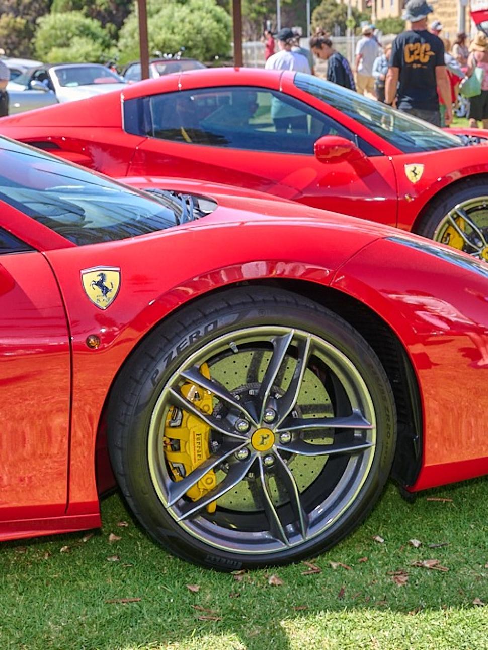Two stunning bright red super cars showcased on a grassed area. There are people in the background admiring the cars. 