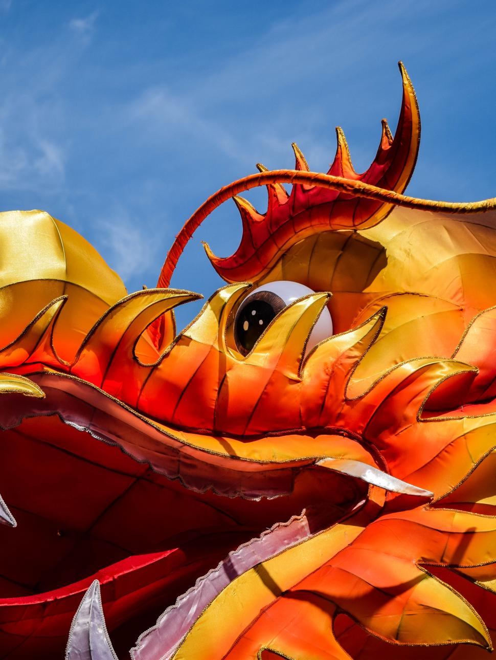 Bright red, orange and gold ornate dragon head with large nostrils and open mouth looking spectacular with blue sky behind it.  