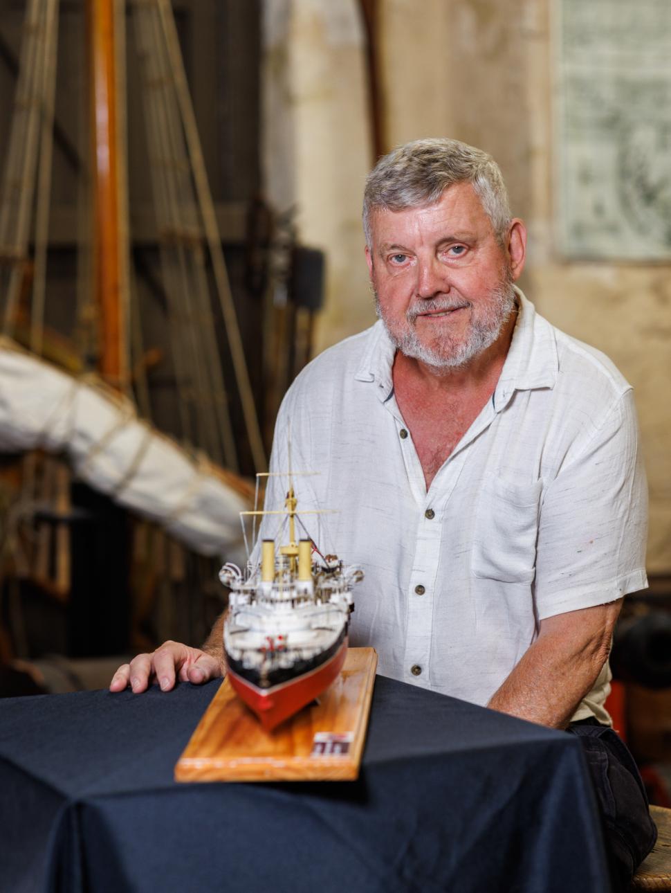 a person sits on a chair with a smile on their face and in front of them is a table with a model ship 