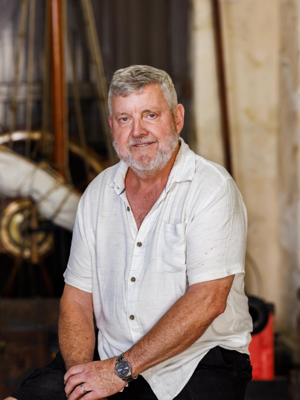 a an adult man sits on a stool smiling with nautical themed props in the background