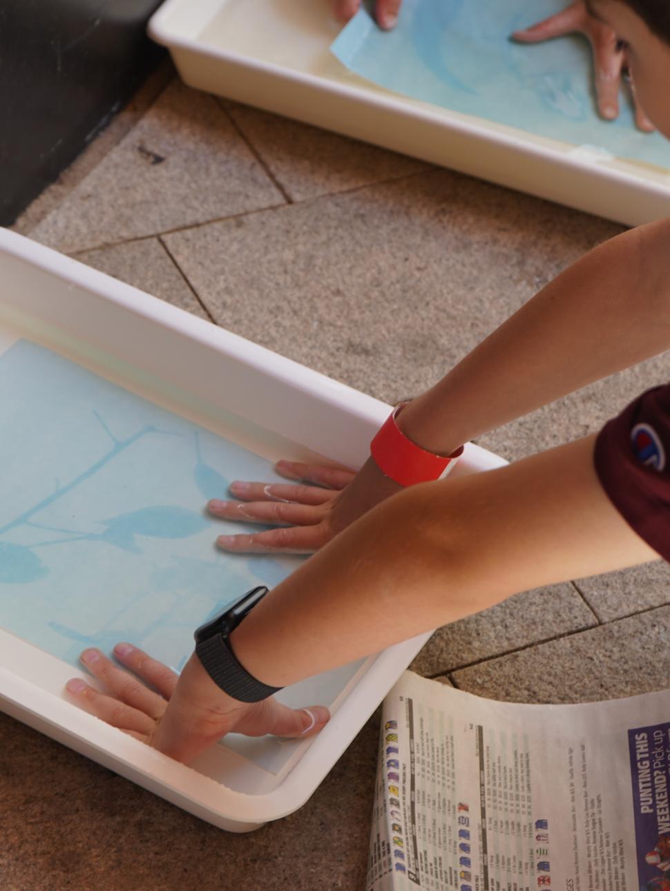 Child washing sun print in tray of water
