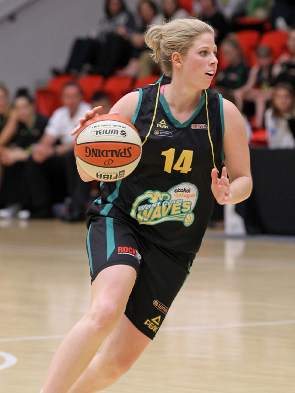 Basketball player, Melissa Marsh in a West Coast Waves uniform dribbling a ball on an indoor court.