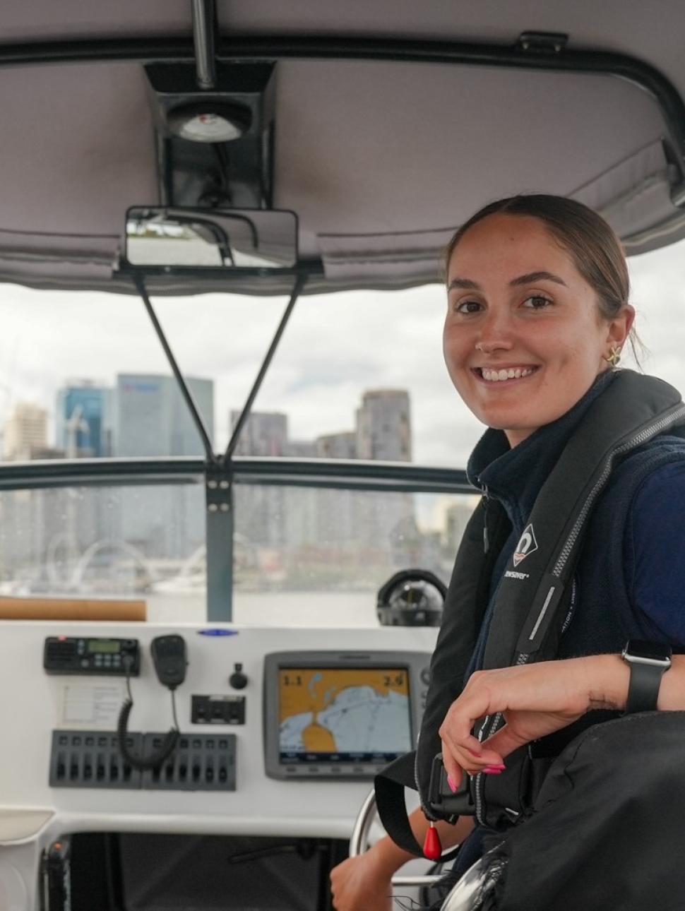 Two female Marine Rangers from WA's Department of Biodiversity, Conservation and Attractions shown at work on a patrol boat on the Swan River in front of the Perth city skyline.