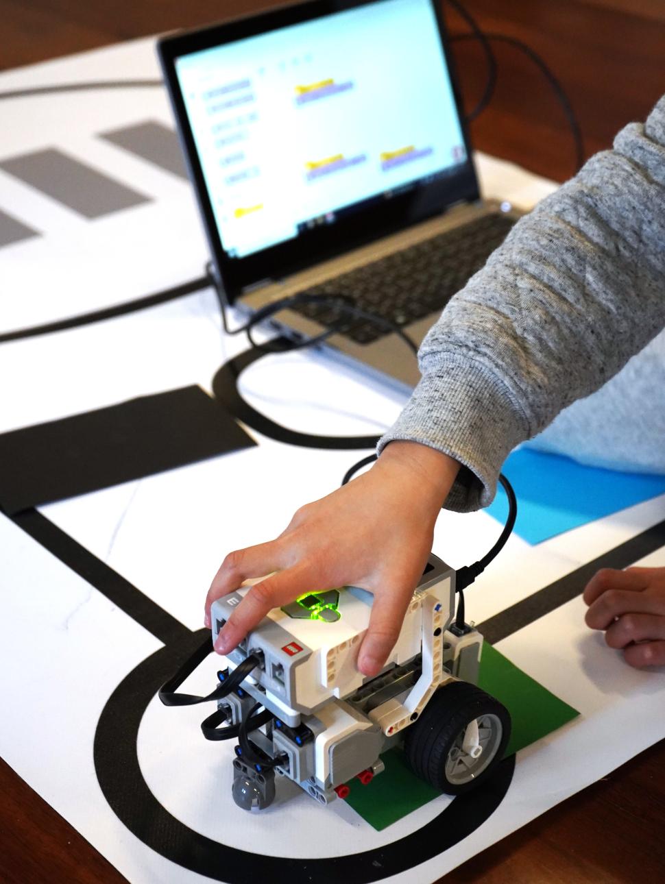 child's hand on EV3 robot with laptop in the background
