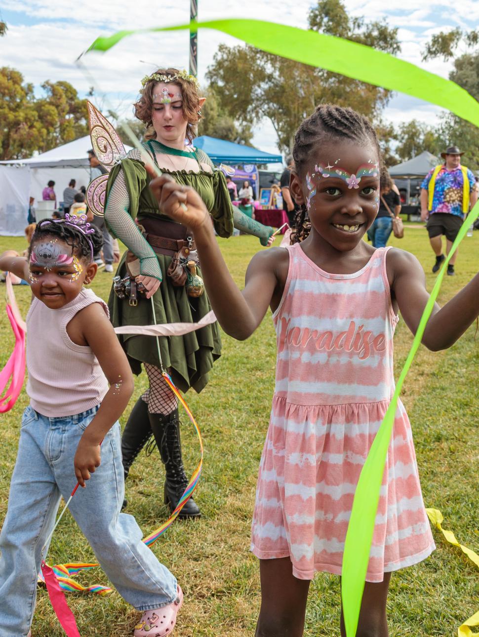children playing outdoors in a park with streamers. They have their face painted and are having a great time smiling