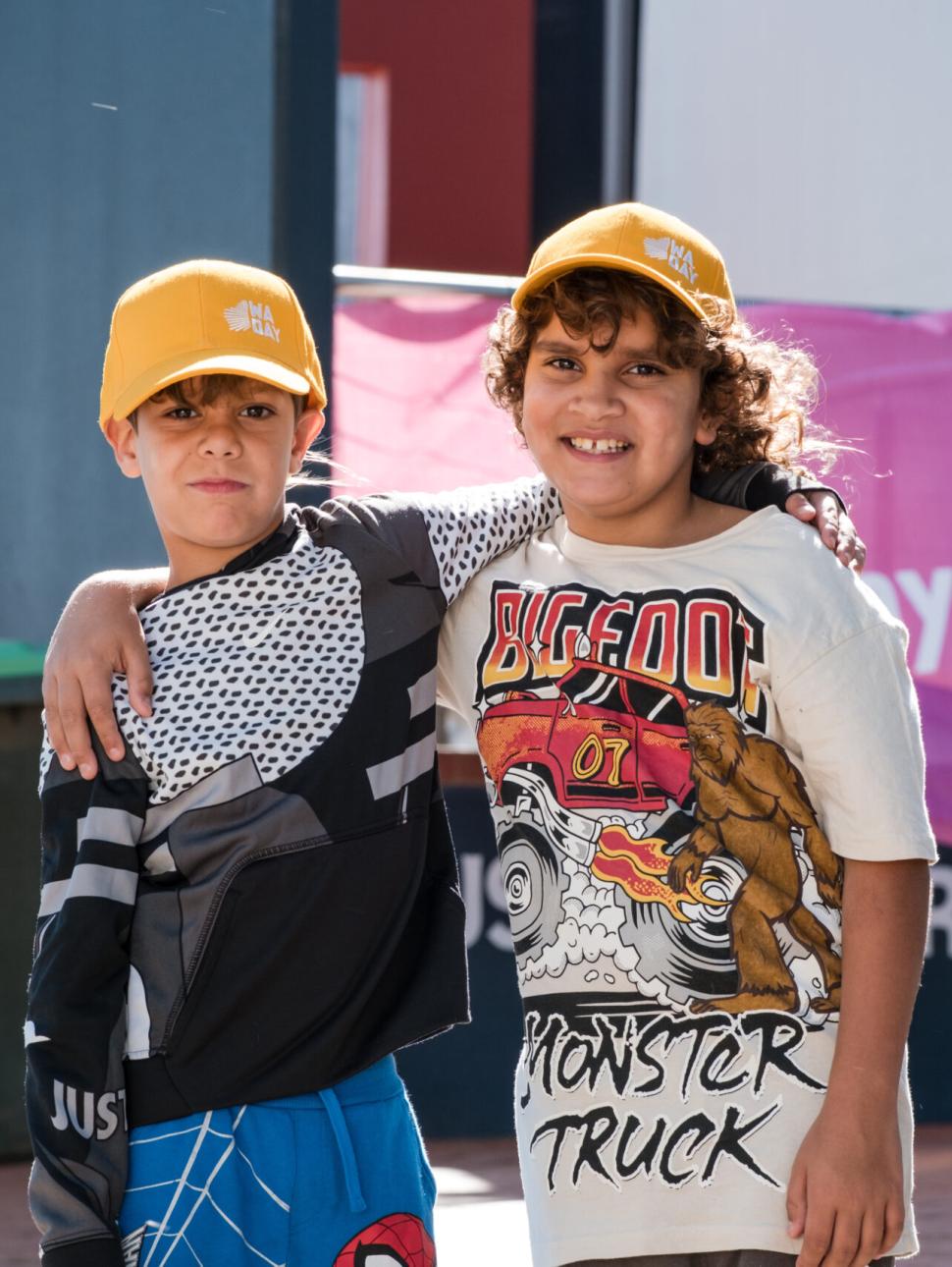two children smiling and happy with yellow hats on and have one arm around eachothers shoulders 
