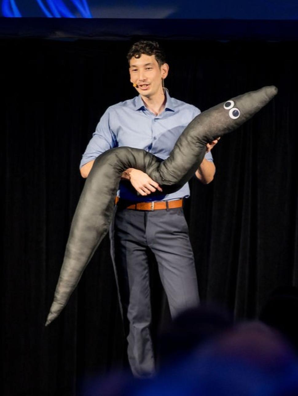Man on stage holding large worm-like soft toy