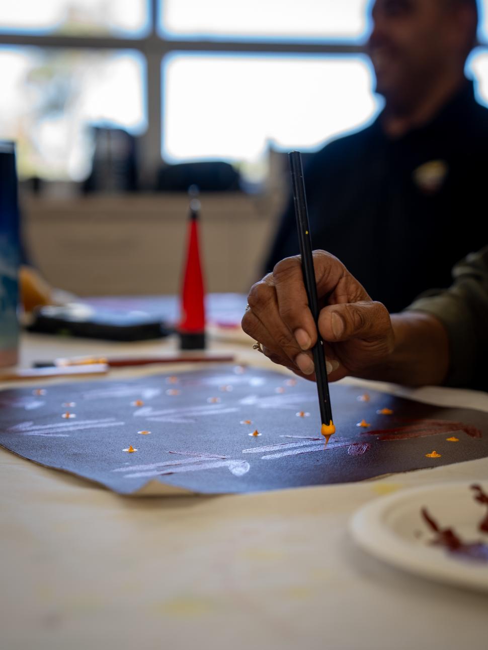a close up of someone painting as they hold the painting tool dipped in yellow paint ready to apply to the paper