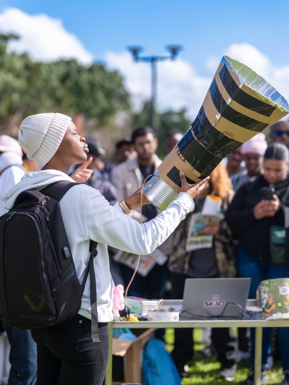 a crowd of people outdoors wher one person holds a tabletop telescope
