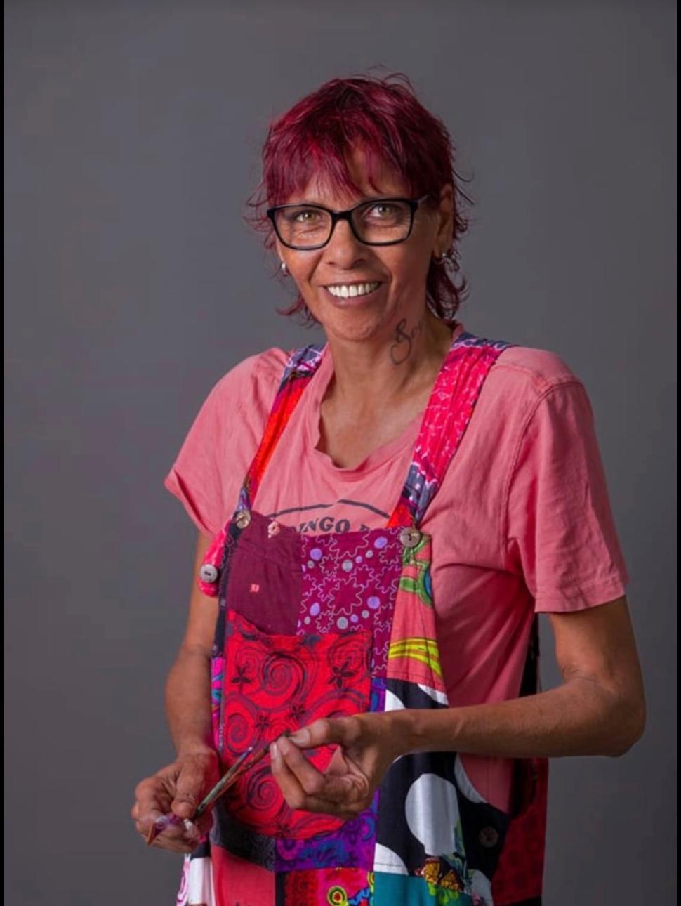 a person looking at the camera with a sincere expression. They were bright coloured clothing and hold art tools in their hands