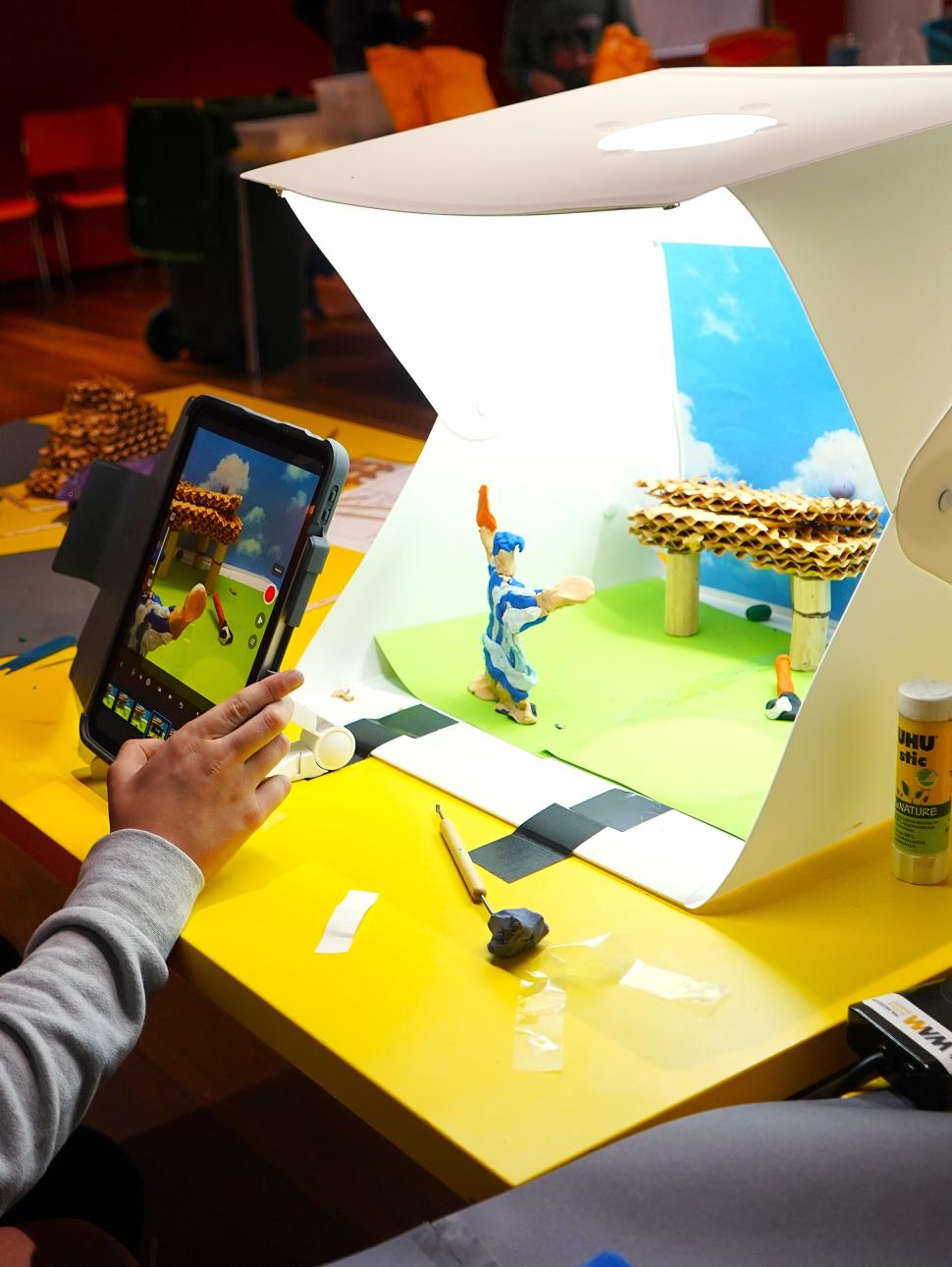 child holding ipad and making a stop motion movie on the table with plasticine characters
